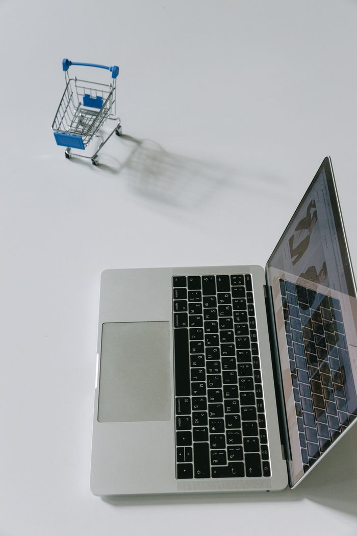 mobile-01 Minimalist scene of a laptop beside a miniature shopping cart symbolizing online shopping.